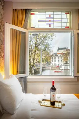 a bottle of wine and two glasses on a bed with a window at Hotel Oscar in Amsterdam