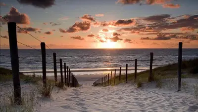 a pathway to the beach with the sunset in the background at Klein Langeveld in Noordwijkerhout