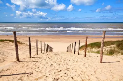 a sandy beach with a fence in front of the ocean at Petite Maison Bennebroek in Bennebroek