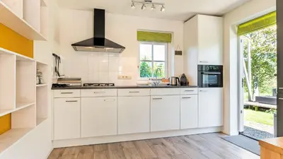a kitchen with white cabinets and a large window at Huisje Avondrood in Schoorl