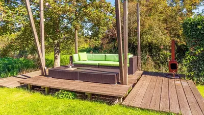 a gazebo with a green couch on a wooden deck at Huisje Avondrood in Schoorl
