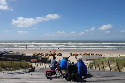 a group of people sitting on a pier looking at the beach at Droomvakanties Egmond Appartement van Speijk in Egmond aan Zee