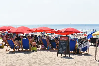 a group of people sitting in chairs and umbrellas on a beach at Droomvakanties Egmond Appartement van Speijk in Egmond aan Zee
