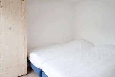 a bedroom with a white bed and a wooden cabinet at klaproos Bergen NH in Bergen