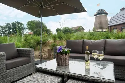 a patio with a table with wine glasses and an umbrella at Zicht op de Molen by Droomvilla in Egmond aan den Hoef