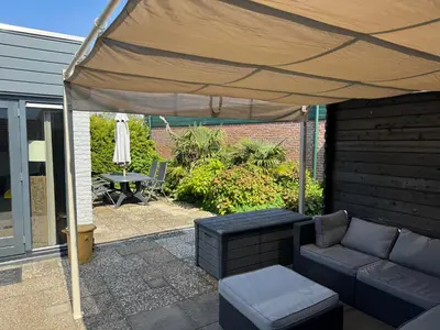 a patio under a tent with a couch and a table at Casa The Wave with infrared sauna in Noordwijkerhout