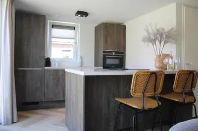 a kitchen with wooden cabinets and a counter with chairs at Buiten aan zee by Droomvilla in Sint Maarten