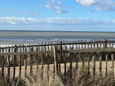 a wooden fence on a beach next to the ocean at Appartement met frontaal zeezicht in Bloemendaal in Bloemendaal