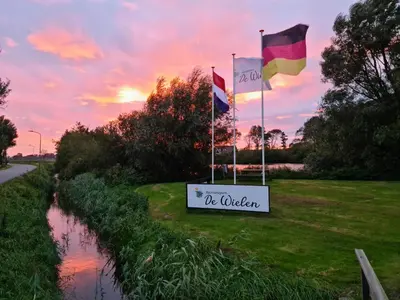 three flags on the side of a river with a sign at Chalet 575 op Recreatiepark De Wielen in Sint Maarten