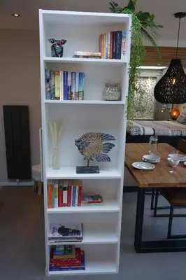 a white book shelf filled with books next to a table at Quetzal in Schoorl