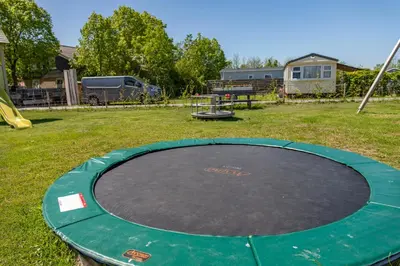 a circular trampoline in a yard with a playground at Chalet 2a op Recreatiepark De Wielen in Sint Maarten