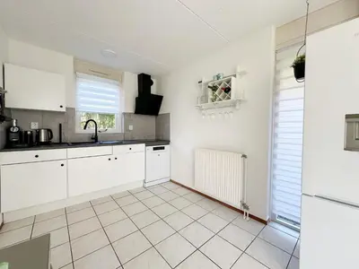 a kitchen with white cabinets and a tile floor at Bungalow 36 op Recreatiepark De Wielen in Sint Maarten