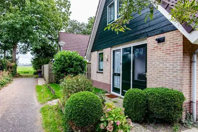 a brick house with a green roof and bushes at Bungalow 40 op Recreatiepark De Wielen in Sint Maarten