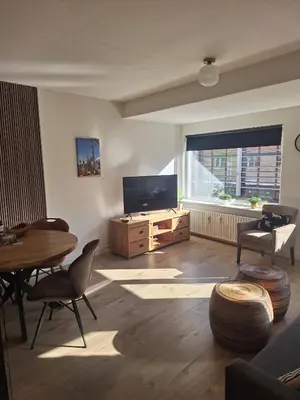 a living room with a television and a table and chairs at Have a nice stay! - Apartment Duinvos 150m from the beach in Noordwijk aan Zee