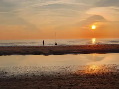 a person standing on the beach at sunset at Vakantiehuis Duinwald, geschikt voor 8 personen in Bergen