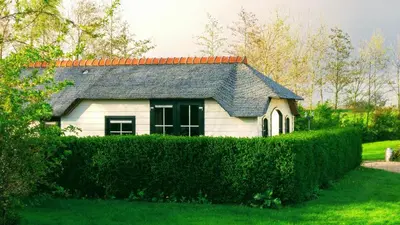 a white house with a hedge in front of it at Mariahoeve-Logies #Polderhuisje in Woubrugge