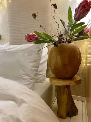 a vase with flowers on a wooden table next to a bed at Casa De Palmas - Tiny house in Alkmaar