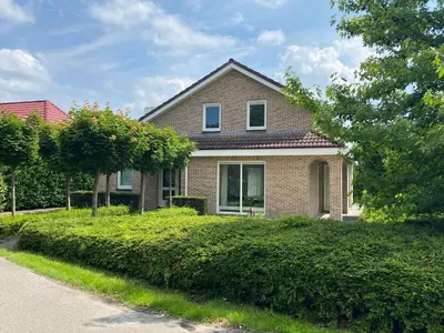 a brick house with bushes in front of a street at Big Family villa 12p big garden with bathtub and jacuzzi in Zeewolde