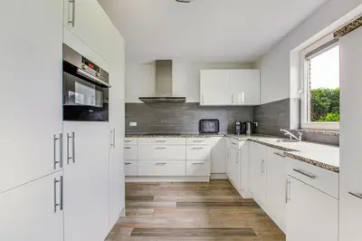 a white kitchen with white cabinets and a window at Big Family villa 12p big garden with bathtub and jacuzzi in Zeewolde