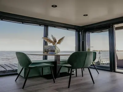 a dining room with a table and two green chairs at Luxury Houseboat Getaway in Uitgeest