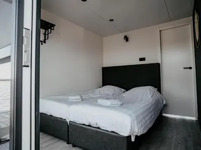 a small bedroom with a bed with white sheets at Luxury Houseboat Getaway in Uitgeest