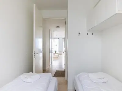 two beds in a room with white walls and a hallway at De Kreeft in Egmond aan Zee