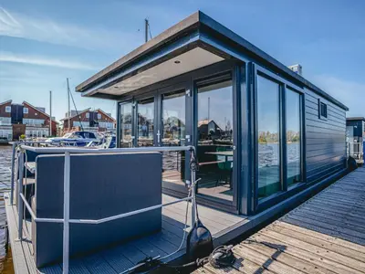 a small house on a dock with glass doors at Tiny houseboat Parel I - airco in Uitgeest