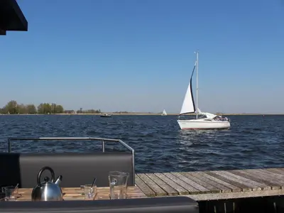 a sailboat on the water with a table and a boat at Tiny houseboat Uitgeest I in Uitgeest