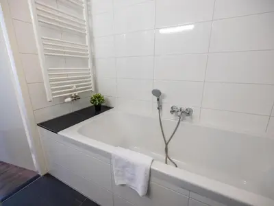 a white bath tub in a white tiled bathroom at Appartement Assum I in Uitgeest