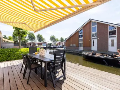 a wooden deck with a table and chairs and a boat at Appartement Assum I in Uitgeest