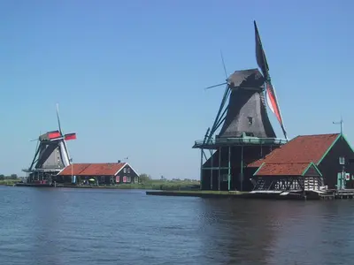 two windmills on the water next to a house at Woonark De Woude in Uitgeest