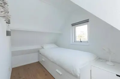 a white bedroom with a bed and a window at Have a nice stay! - Salty Beachhouse in Noordwijk aan Zee