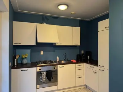 a kitchen with white cabinets and a blue wall at Zwaan 24-7 in Breukelen