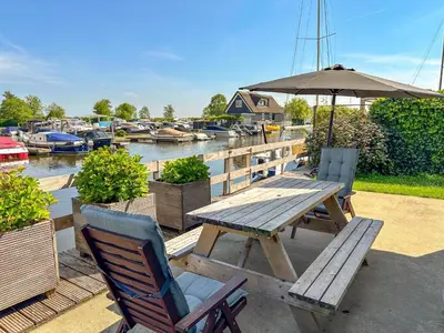 a picnic table with chairs and an umbrella next to a marina at Zwaan 24-7 in Breukelen