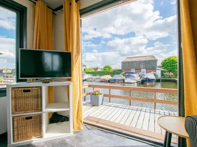 a living room with a tv and a balcony with boats at Blauwborst 24-20 in Breukelen