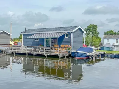 a blue house on a dock with a boat on the water at Purperreiger 24-32 in Breukelen