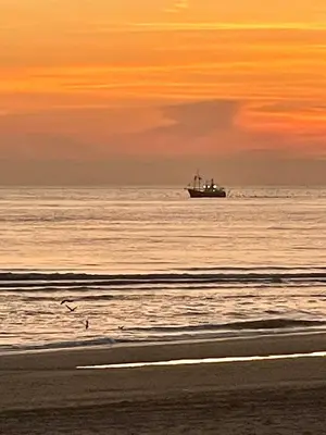a boat in the ocean at sunset with a beach at Comfortable Room in Alkmaar