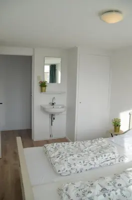 a white bedroom with a bed and a sink at Seapaerdje in Bergen aan Zee