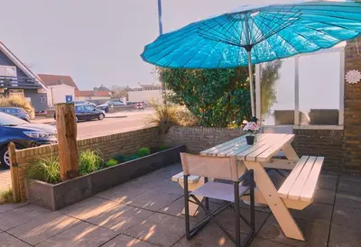 a picnic table with a blue umbrella and a bench at Seapaerdje in Bergen aan Zee