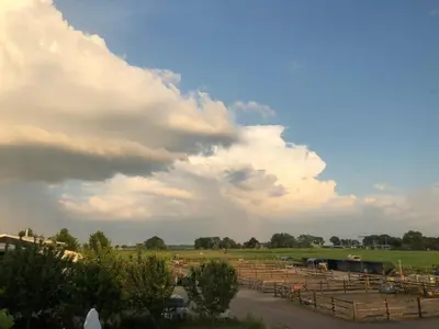 a cloudy sky over a farm with cows in a field at Hestar Husid, het luxe paardenhuis in Weesp