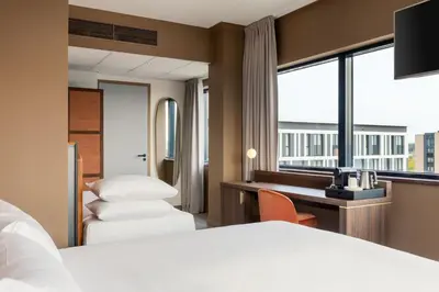 a hotel room with two beds and a desk and a window at Corendon Amsterdam Schiphol Airport, a Tribute Portfolio Hotel in Badhoevedorp