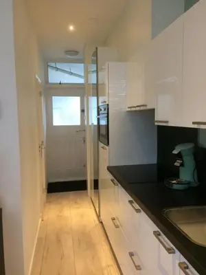 a kitchen with white cabinets and a glass door at De Wulk 26 in Zandvoort