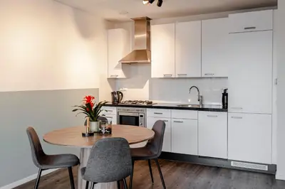 a kitchen with white cabinets and a wooden table and chairs at Kaag Resort in Warmond