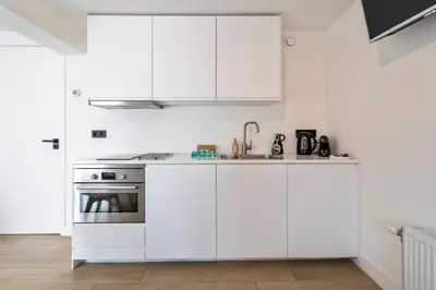 a white kitchen with white cabinets and a sink at Studio Thor, With free parking in Zandvoort