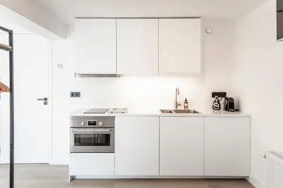 a white kitchen with white cabinets and a stove at Studio Thor, With free parking in Zandvoort
