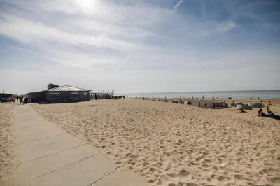a sandy beach with a building and people on it at De Kroft Beach Residences Noordwijk aan Zee in Noordwijk
