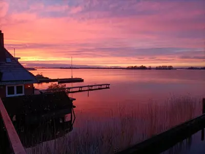 a sunset over a lake with a house and a dock at Plassenzicht Logies & Sloepverhuur in Loosdrecht