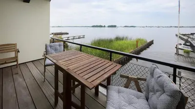 a balcony with a table and chairs and a view of a lake at Plassenzicht Logies & Sloepverhuur in Loosdrecht