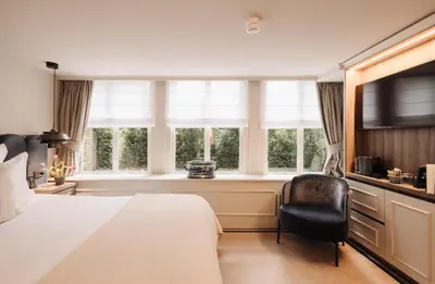 a bedroom with a bed and a chair and windows at Hotel 717 in Amsterdam