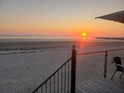 a sunset on the beach with a deck and chairs at Zeelicht in Noordwijkerhout